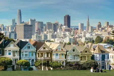 Picnickers sit on the grass at Alamo Square Park with the Painted Ladies and San Francisco skyline in the background.